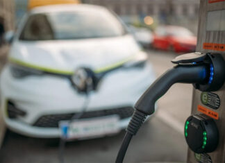 An EV charger in focus with an electric car in the background