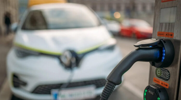 An EV charger in focus with an electric car in the background