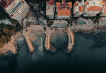 Aerial view of a part of the coastline of Puerto Vallarta, featuring beachfront homes in bright orange and white and pools of various shapes.