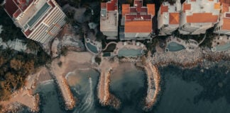 Aerial view of a part of the coastline of Puerto Vallarta, featuring beachfront homes in bright orange and white and pools of various shapes.