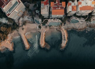 Aerial view of a part of the coastline of Puerto Vallarta, featuring beachfront homes in bright orange and white and pools of various shapes.