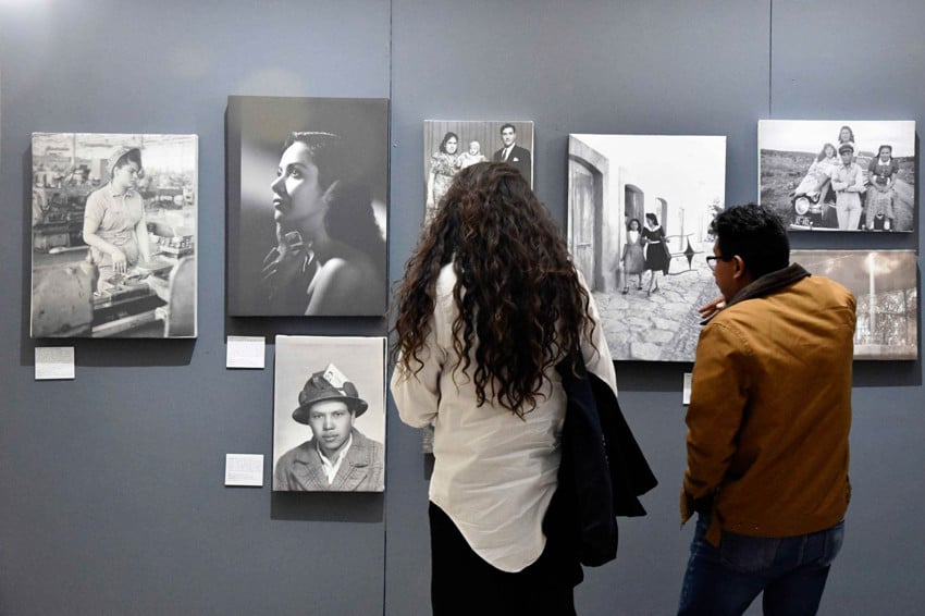 Two Mexicans, a woman with long hair in a white blouse and black slacks and a man with a beige winter jackets are standing with their back to the camera as they look at photos on display at a photography exibition in a museum in Zacatecas, Mexico.