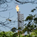 A large gas flare visible through trees at Olmeca Refinery in Dos Bocas, Tabasco.