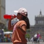 Mexican girl in a orange tee shirt and pink baseball cap drinks a Gatorade bottled energy drink in Guadalajara's historic center.