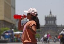 Mexican girl in a orange tee shirt and pink baseball cap drinks a Gatorade bottled energy drink in Guadalajara's historic center.