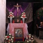 A Viernes de Dolores altar to the Virgin Mary is on display in a San Miguel de Allende resident's garage. The creator, a Mexican woman in jeans, a jacket and cap, is standing by the altar with her young son, also dressed in warm clothes. He is holding a small tray of popsicles to give to visitors.