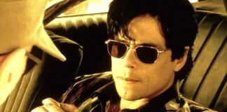 Benecio del Toro in dark aviator sunglasses sitting in a car, in a scene from the film "Traffic."