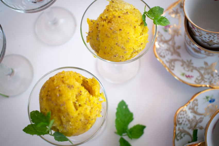 wo scoops of mango sorbet with chia seeds served in small wineglasses or desert cups, garnished with fresh mint leaves next to vintage ceramic teacups and saucers.