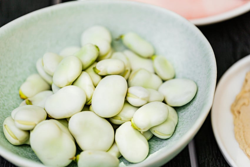 A light blue bowl filled with fresh, peeled fava beans (habas), a staple ingredient in traditional Mexican soups and salads.