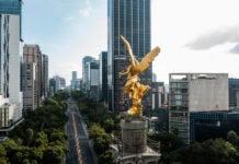 A view over the shoulder of the golden Angel of Independence statue in Mexico City, looking down Paseo de la Reforma