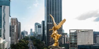 A view over the shoulder of the golden Angel of Independence statue in Mexico City, looking down Paseo de la Reforma