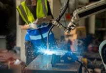 A robotic arm solders delicate electronics as an engineer looks on