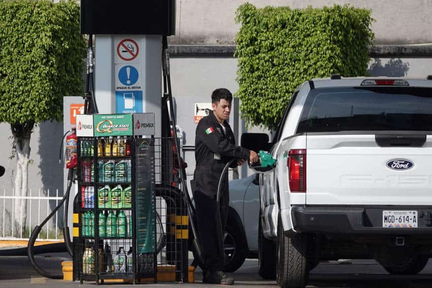 Mexican Pemex gas station employee in a black uniform with a Mexican flag on it pumps gas into a white Ford pickup truck in Mexico City, which is facing rising food prices