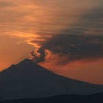 Small clouds of ash from Popocatépetl volcano catch the light of the rising sun