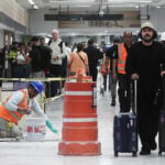Passengers walk past orange construction cones and a construction worker in Mexico City International Airport (AICM)