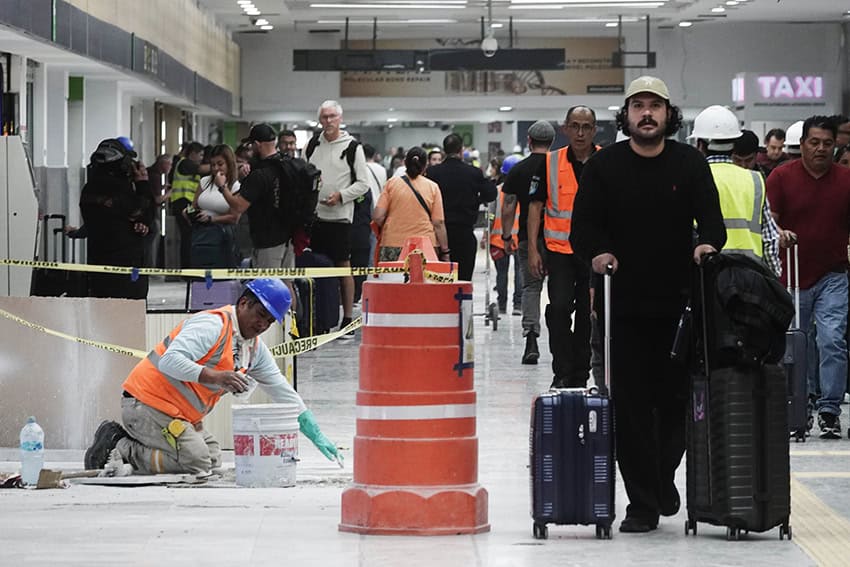 Passengers walk past orange construction cones and a construction worker in Mexico City International Airport (AICM)