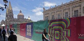 Pedestrians pass a colorful fence with World Cup messaging, with the Guadalajara cathedral in the background