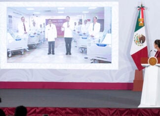 Sheinbaum stands before a podium and views a presentation by her government's Health Ministry