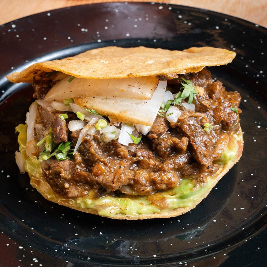 A hearty meat taco with cilantro and onion between two fried tortillas, on a black plate with a white speckled design.