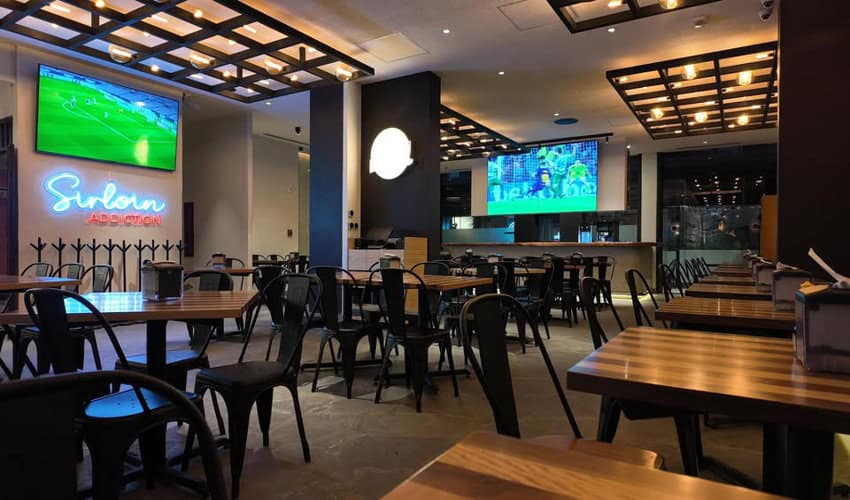 A causal taco restaurant in Mexico City with pub-style tables and chairs. Two large-screen tvs are on in the background, showing sports games.