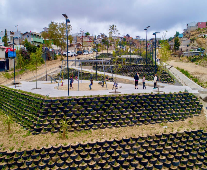 Children and adults on a raised playground created by hundreds of used tires arranged in a pyramid style shape that serves as a base for the playground. The tires are filled with live plants.