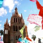 colorful paper papel picado flags fly around the cathedral of San Miguel de Allende