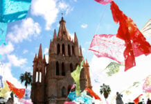 colorful paper papel picado flags fly around the cathedral of San Miguel de Allende