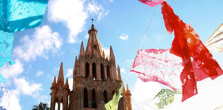 colorful paper papel picado flags fly around the cathedral of San Miguel de Allende