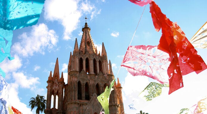 colorful paper papel picado flags fly around the cathedral of San Miguel de Allende