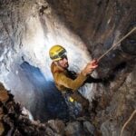 A man rappels down into a cave