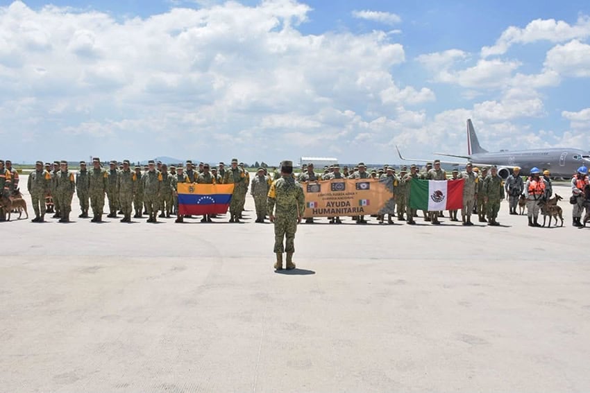 Mexican troops pose with search and rescue dogs, a Venezuela and Mexican flag, and a sign reading Ayuda Humanitaria