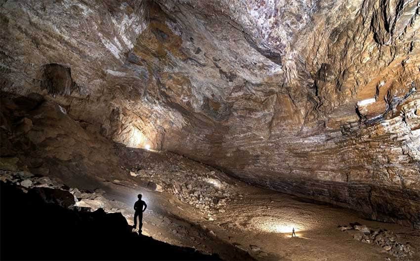 A man stands silhoutteted in a cave.