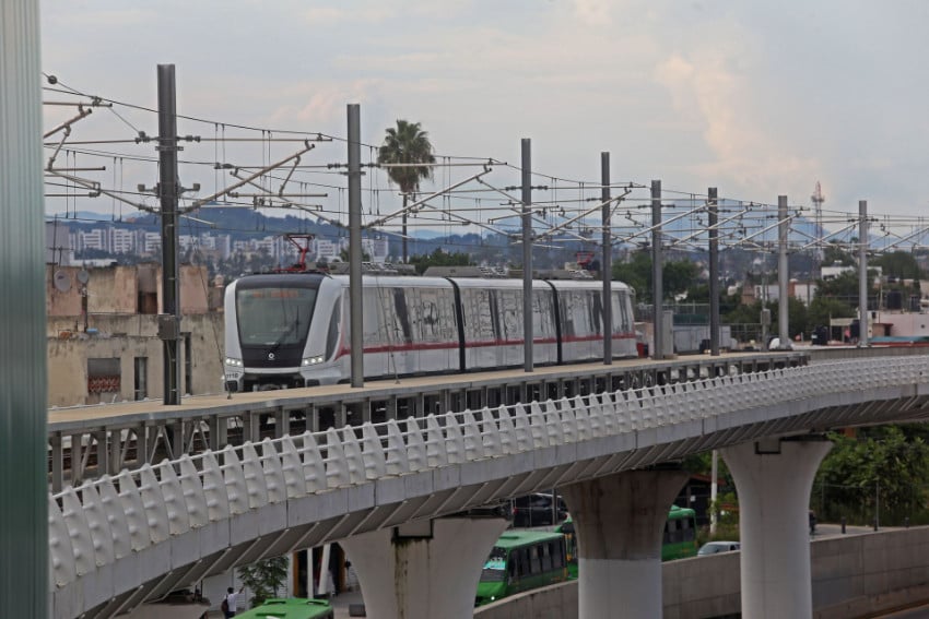 A light-rail train crossing a white and gray bridge in Zapopan, Jalisco, in Mexico. In the background is the cityscape of Zapopan.
