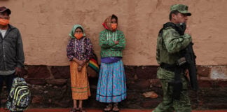 Two women in traditional Rarámuri dress watch as National Guard members patrol the town of Cerocahui in the mountainous region of Chihuahua known as the Sierra Tarahumara.