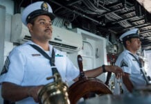 Two uniformed Mexican navy personnel at the helm of a Mexican navy ship. One man has his hand resting on the ship's steering wheel