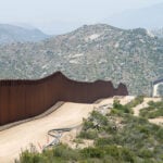 The Mexico-US border wall cuts through an arid mountainous landscape