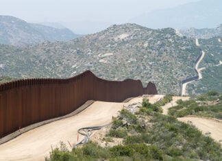 The Mexico-US border wall cuts through an arid mountainous landscape