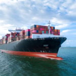 Aerial side view of cargo ship carrying shipping containers for export
