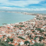 Coastline of Puerto Vallarta during the daytime, densely packed with similar white and red adobe multistory buildings.