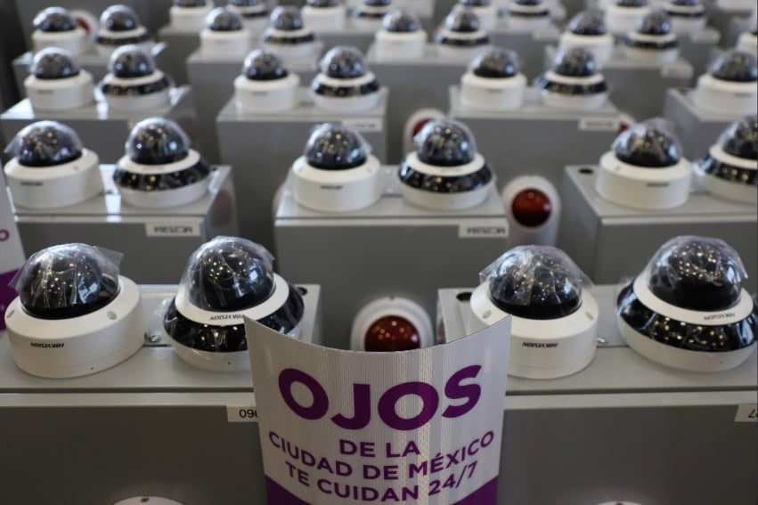A placard reading "Mexico City's eyes protect you 24/7" at the rollout of the Ojos que te cuidan digital surveillance program, next to security cameras