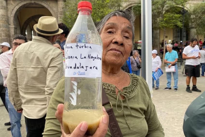 Woman holding up bottle of dirty Guadalajara tap water at demonstration.