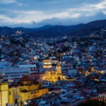 Cathedral and historic buildings lit up in a view of Guanajuato's Zona Centro neighborhood at dusk.