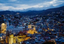 Cathedral and historic buildings lit up in a view of Guanajuato's Zona Centro neighborhood at dusk.