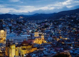 Cathedral and historic buildings lit up in a view of Guanajuato's Zona Centro neighborhood at dusk.