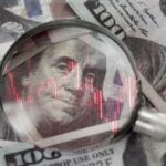 red downward arrow inside a magnifying glass placed over a U.S. dollar banknote symbolizes economic decline, financial crisis, or recession in the United States.