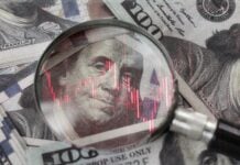 red downward arrow inside a magnifying glass placed over a U.S. dollar banknote symbolizes economic decline, financial crisis, or recession in the United States.