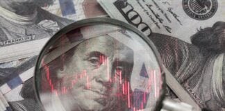 red downward arrow inside a magnifying glass placed over a U.S. dollar banknote symbolizes economic decline, financial crisis, or recession in the United States.