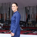 President Sheinbaum smiles in front of a pile of confiscated firearms