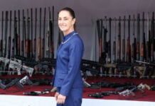 President Sheinbaum smiles in front of a pile of confiscated firearms