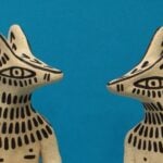 Two biege sculptures featuring what appears as dogs with black painted markings on blue background